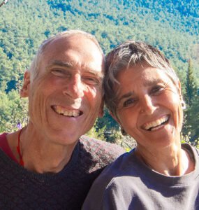 A lovely portrait of Asli and John smiling in front of a tree-covered hill on a sunny day at the Valley of Breath.