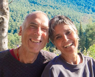 A lovely portrait of Asli and John smiling in front of a tree-covered hill on a sunny day at the Valley of Breath.