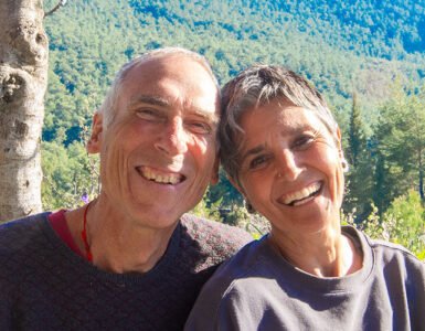 A lovely portrait of Asli and John smiling in front of a tree-covered hill on a sunny day at the Valley of Breath.