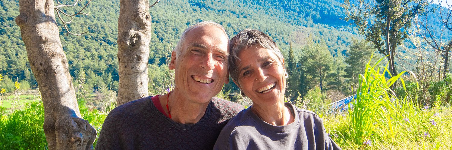 A lovely portrait of Asli and John smiling in front of a tree-covered hill on a sunny day at the Valley of Breath.