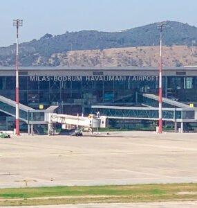 Exterior view of Milas-Bodrum Airport terminal with parked aircraft and boarding gates.