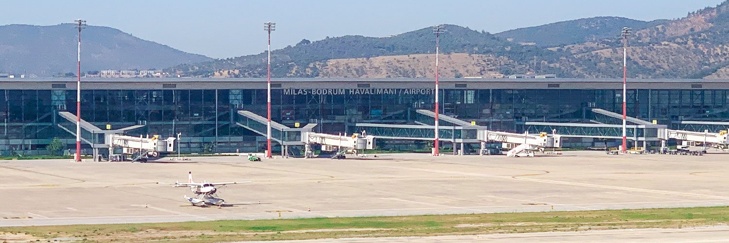 Exterior view of Milas-Bodrum Airport terminal with parked aircraft and boarding gates.