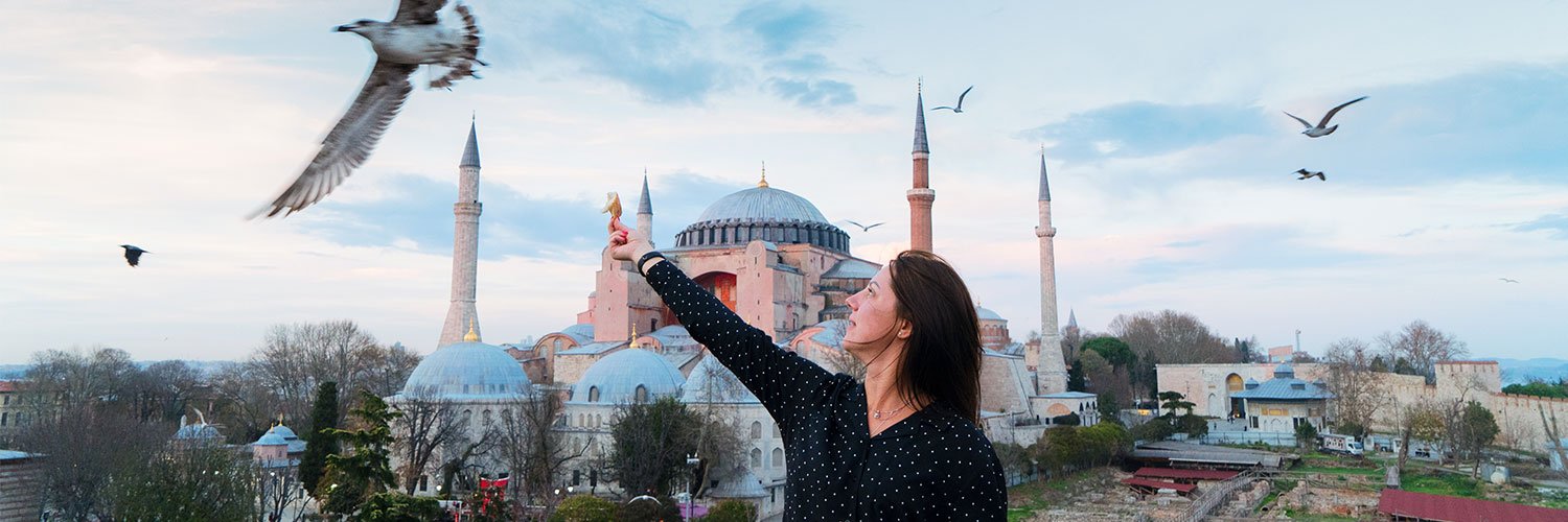 A woman feeding birds in front of the historic Hagia Sophia in Istanbul, showcasing a blend of Turkish history and culture.