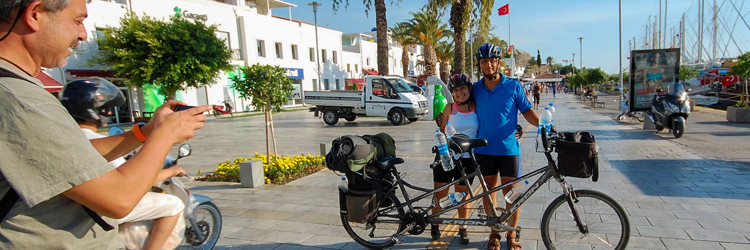 Two travellers on a tandem bicycle posing for a photo at Bodrum Harbour on their Turkey journey.