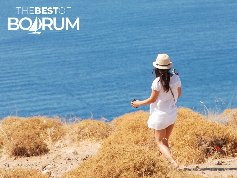 A woman walking toward the sea near the windmills above Bodrum and Gümbet Bays, capturing the relaxed rhythm of the Aegean coast.