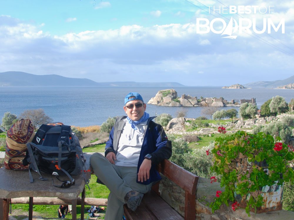 Traveller resting at a village café overlooking Lake Bafa and the ruins of Heraklia during a hike in the Bodrum region.