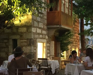 Guests enjoying a sunset dinner at a cosy Bodrum restaurant under leafy trees.