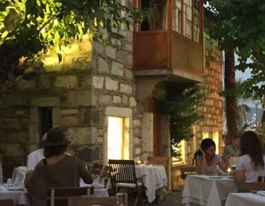 Guests enjoying a sunset dinner at a cosy Bodrum restaurant under leafy trees.