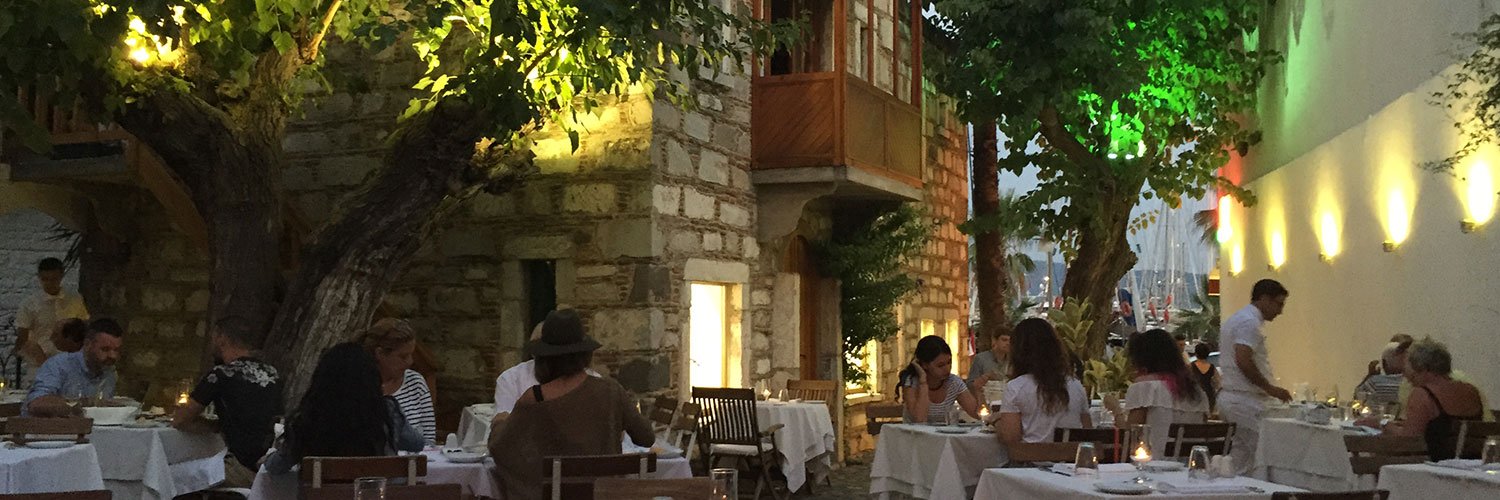 Guests enjoying a sunset dinner at a cosy Bodrum restaurant under leafy trees.