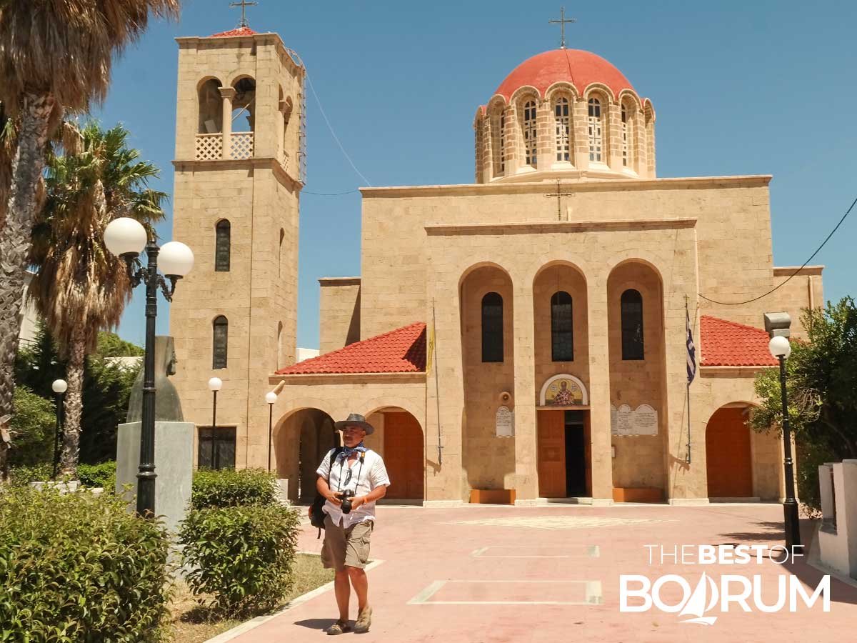 Man holding a camera in front of a church building on Kos Island
